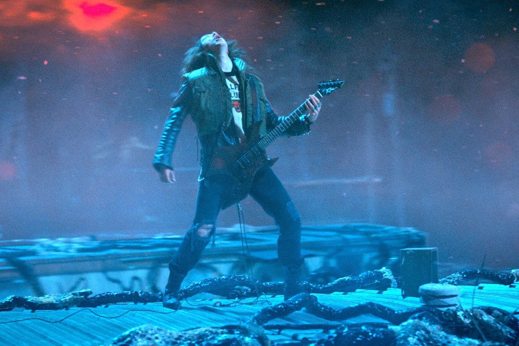 Eddie Munson plays guitar, head thrown back, on the roof in the Upside Down
