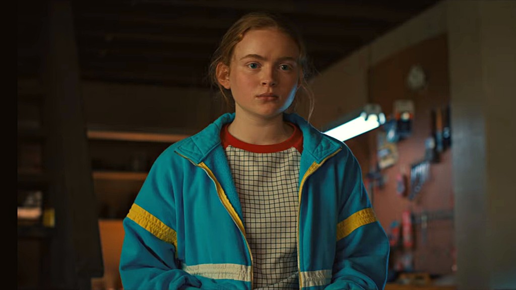 Max Mayfield in a blue jacket with yellow stripes and a red collar, in a workshop