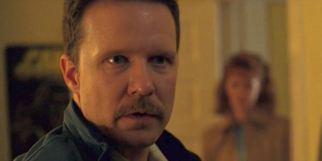 Neil, mustache and dark jacket, in the hallway, Susan blurred behind him.