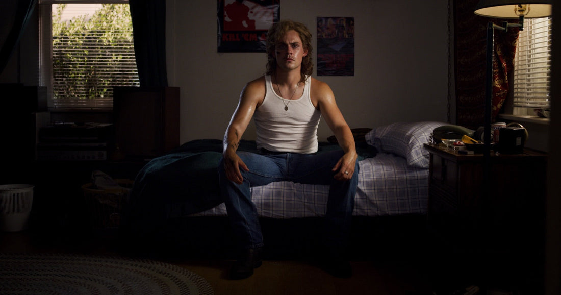 Billy sitting on a bed, chest and arms marked by black veins.