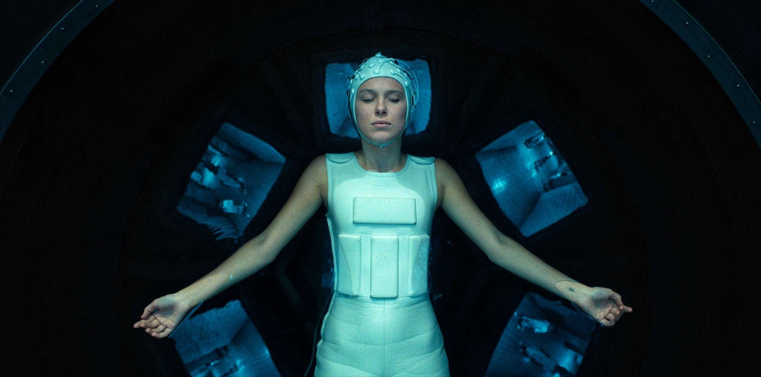 Eleven in the tank, white helmet and suit, with screens around her.