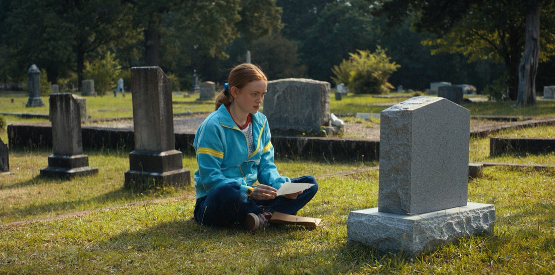 Max sitting in a cemetery, an open letter on her knees, Stranger Things season 4 episode 4